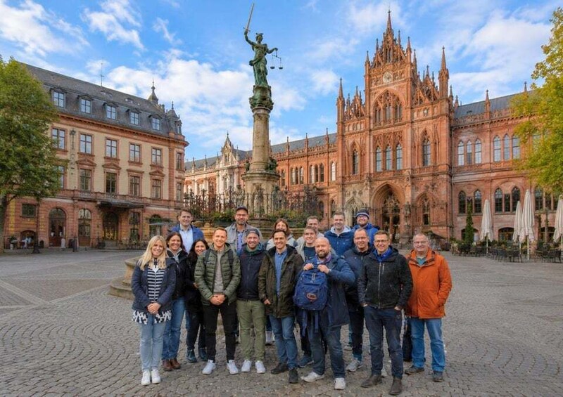 A group of people standing in front of a historic building with a statue in the center. 4
