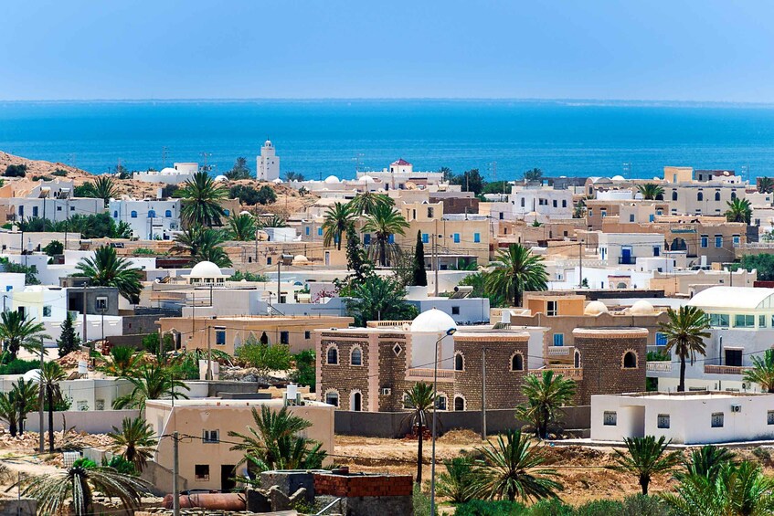 A coastal town with white buildings, palm trees, and a clear blue sea. 4