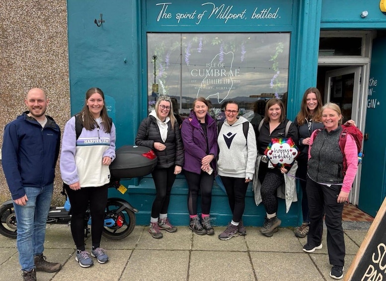 A group of people standing in front of a building with a sign that reads 'The spirit of Millport, bottled.' 3