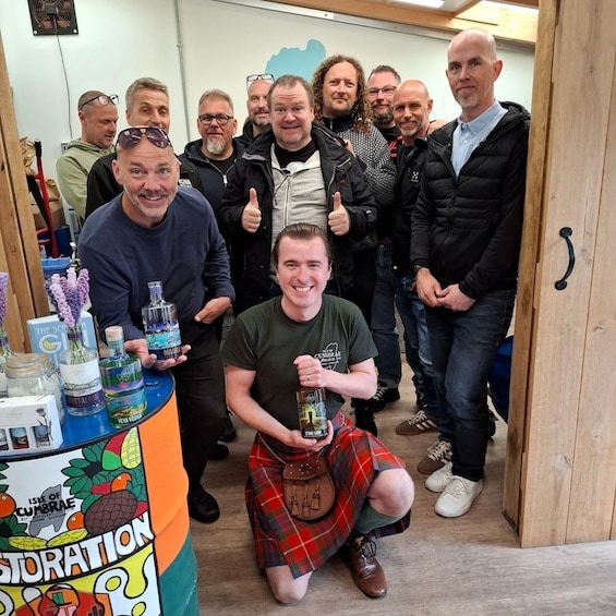 A group of people in a room with a table displaying various bottles and a sign that reads 'Isle of Cumbrae.' 1