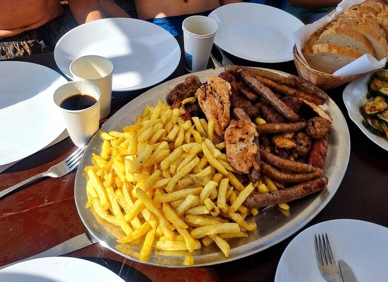 A plate of food with fries, sausages, and grilled chicken, along with a basket of bread and a cup of coffee. 4
