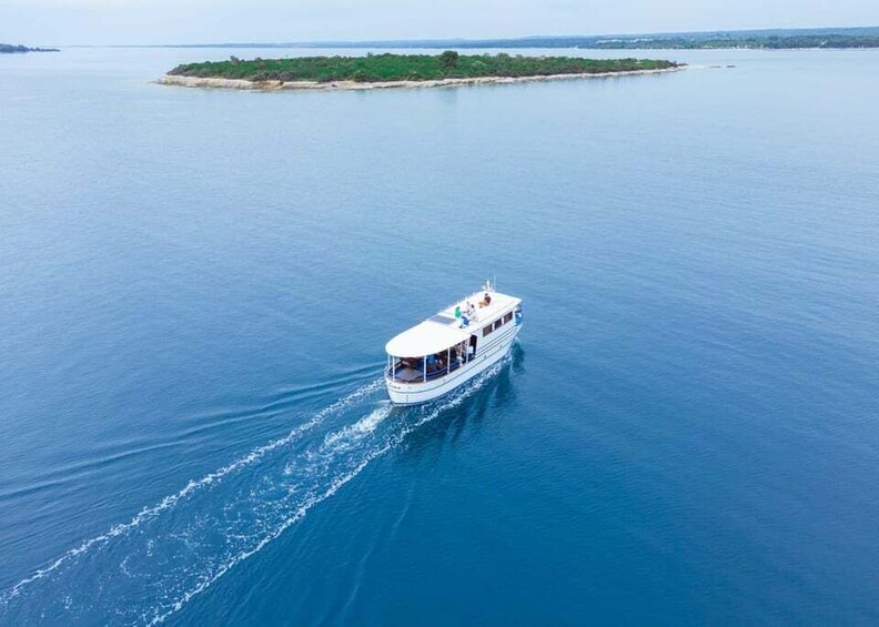 A white boat with a blue stripe on the water, surrounded by calm blue sea and a small island with greenery in the distance. 2