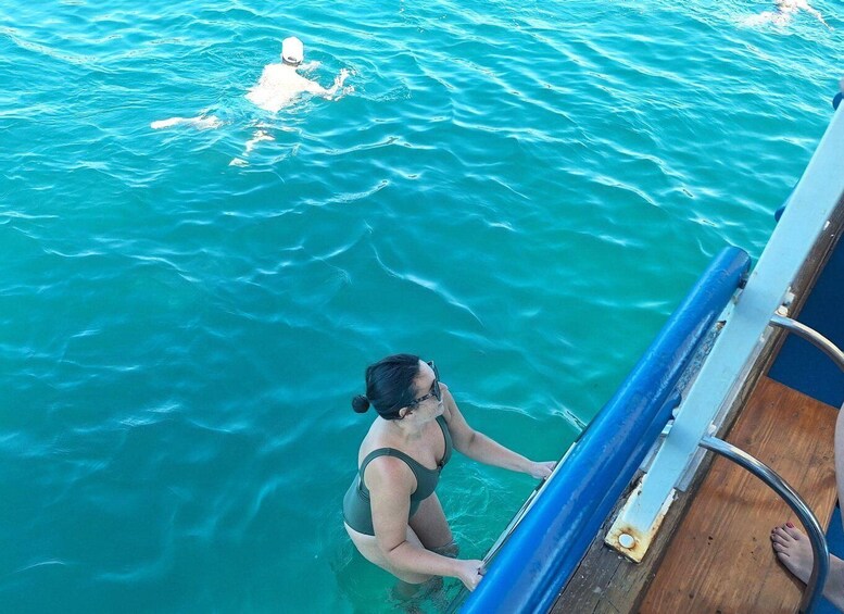 A person in a swimsuit standing at the edge of a boat, looking out over turquoise water. 1