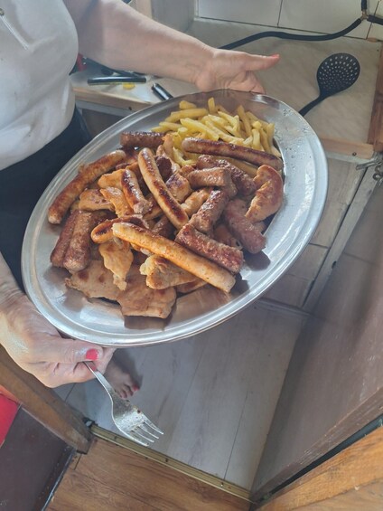 A person holding a plate with grilled sausages, fries, and a piece of flatbread. 4