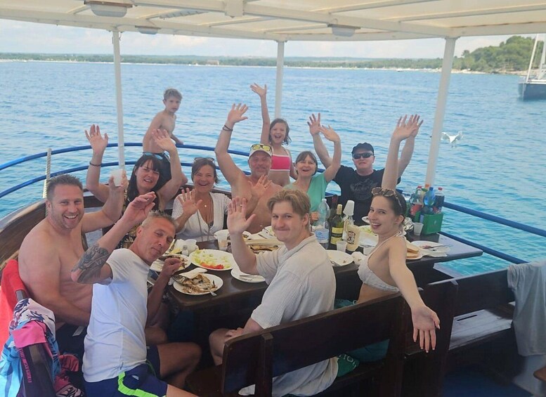 A group of people on a boat with raised hands, dining tables with food, and a body of water in the background. 3