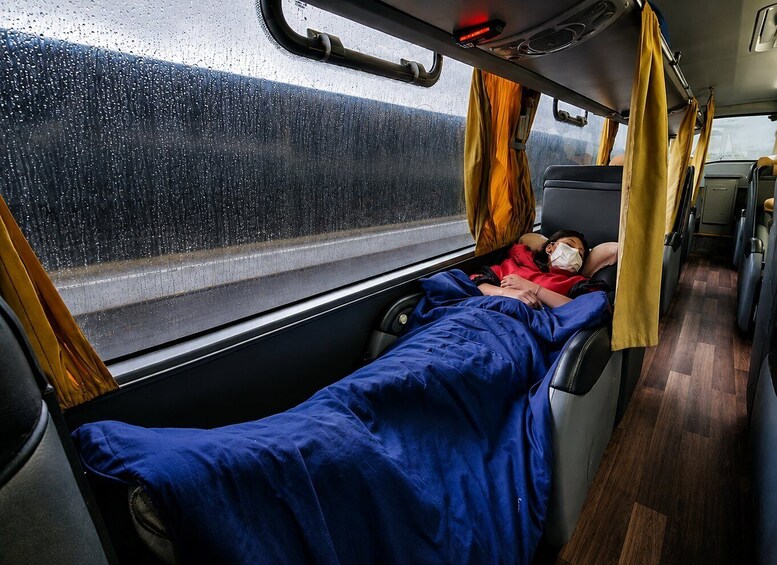 A train interior with a sleeping passenger, a window with raindrops, and yellow curtains. 2