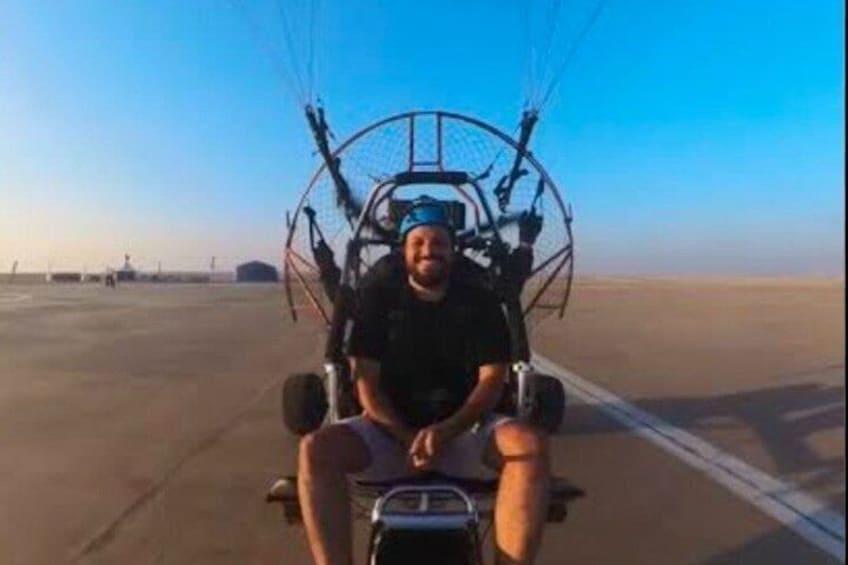 A person in a harness attached to a large, circular, mechanical device on a flat, open surface. 2