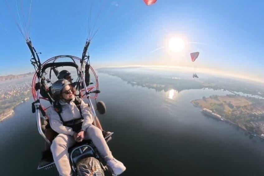 A person in a paragliding harness, a body of water below, and a clear sky. 1