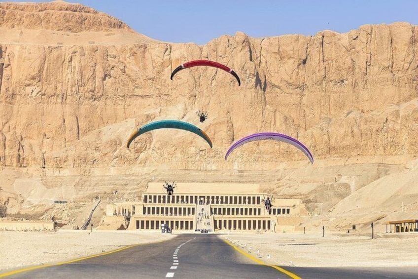 A desert road with three parachutes descending towards a building. 5