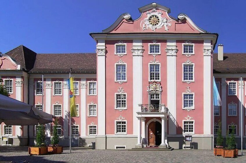 A pink building with white trim and columns, a clock, and flags. 4