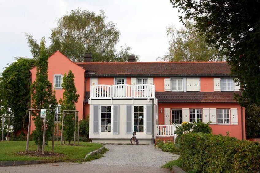 A two-story building with a red facade, white shutters, and a balcony with white railings. 2