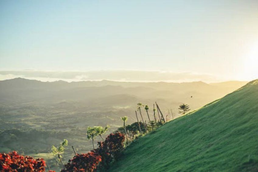 A hilly landscape with a clear sky, distant mountains, and sparse vegetation. 2