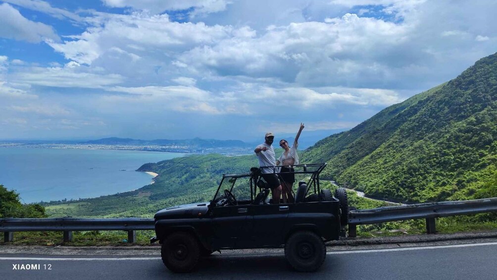 A black off-road vehicle on a road with a coastal landscape and mountains in the background. 3