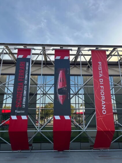 Three banners with text and a red car illustration, mounted on a metal structure in front of a building with large windows. 5