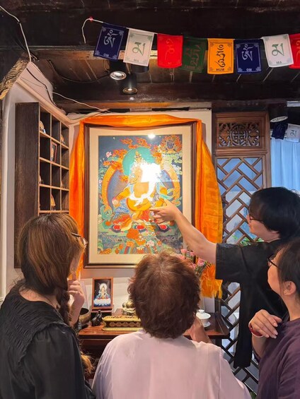 A group of people in a room with a colorful painting and prayer flags. 2