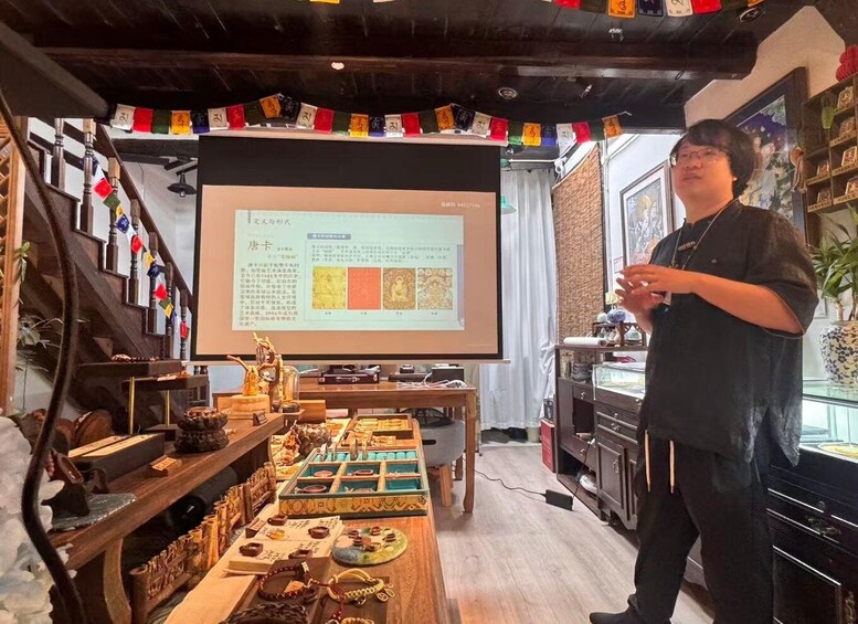 A person presenting in front of a screen with text, surrounded by traditional items and a wooden table with various objects. 4