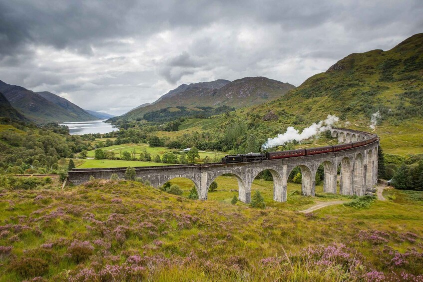 A train on a stone viaduct over a valley with a lake in the background. 2
