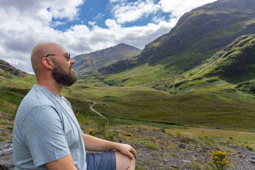 A man sitting on a rock overlooking a mountainous landscape with a winding road. 1