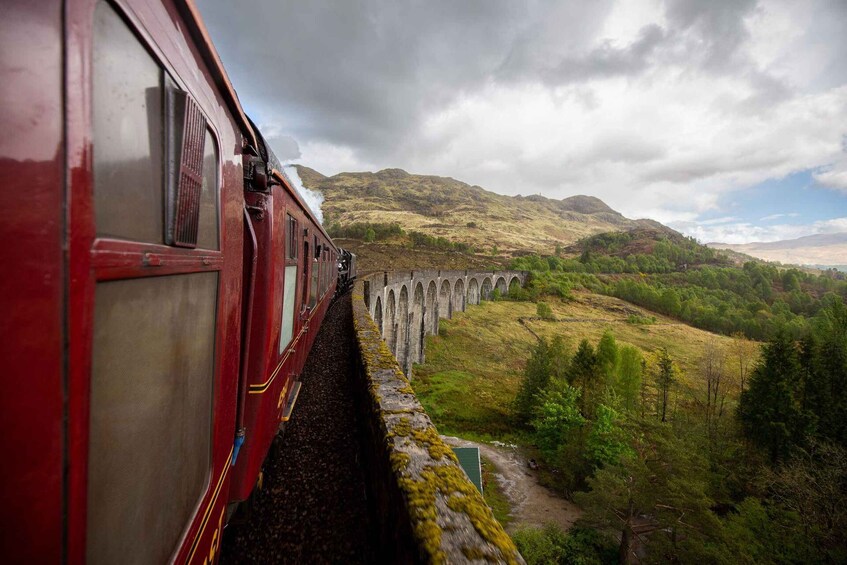 A red train traveling over a stone viaduct through a hilly landscape. 5