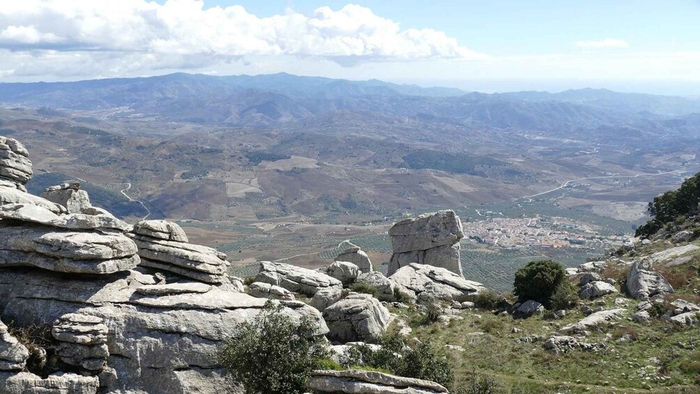 A mountainous landscape with rocky outcrops and a distant view of a valley with a town. 5