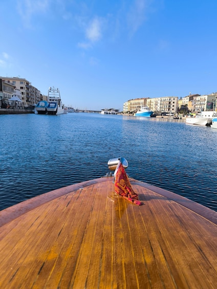 A wooden boat deck with a red and gold cloth, calm water, and buildings along the waterfront. 2