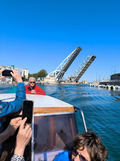 A boat with people taking photos, a bridge in the background, and calm water. 3