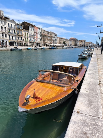 A wooden boat docked at a waterfront with buildings in the background. 1