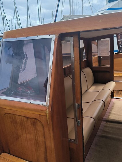 A wooden boat interior with a cushioned bench, a steering wheel, and a window. 5