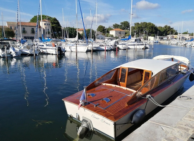 A marina with various boats docked, a wooden boat named 'Sanna Elena' prominently in the foreground, and buildings in the background. 4