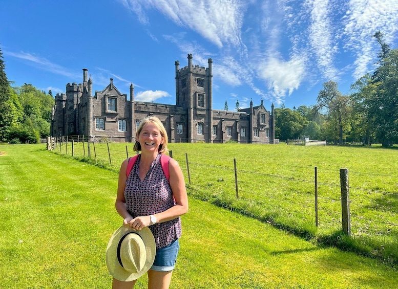 A person standing in front of a large, historic building with a grassy field and a clear blue sky. 1
