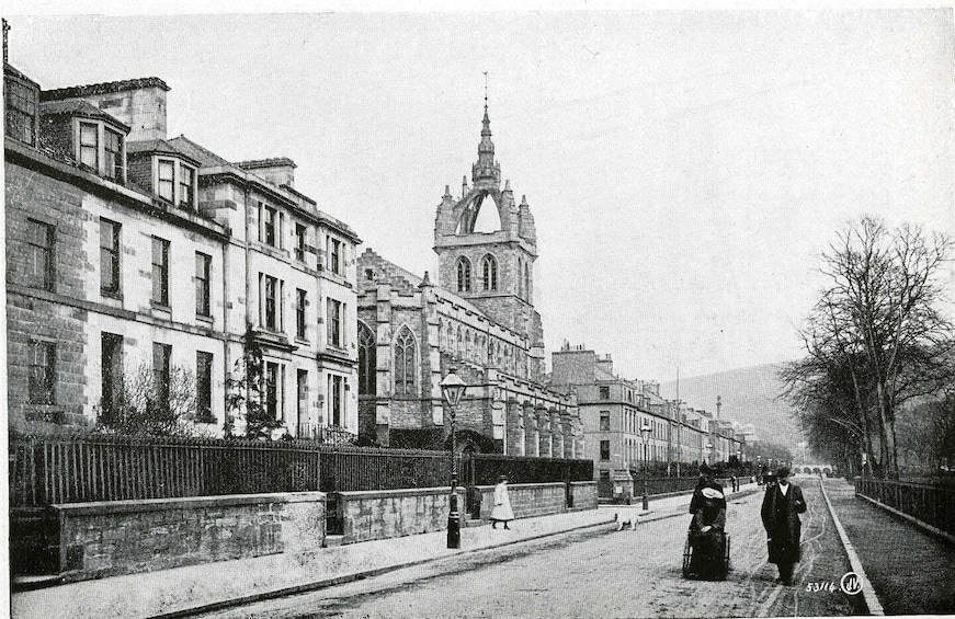A street with historic buildings, a prominent church tower, and pedestrians. 2