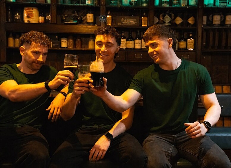 Three people toasting with beer glasses in a bar with shelves of bottles. 4