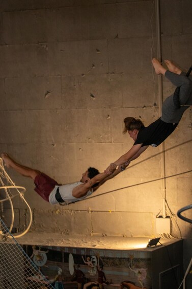 Two people performing an acrobatic act on a rope, with a circus tent in the background. 5