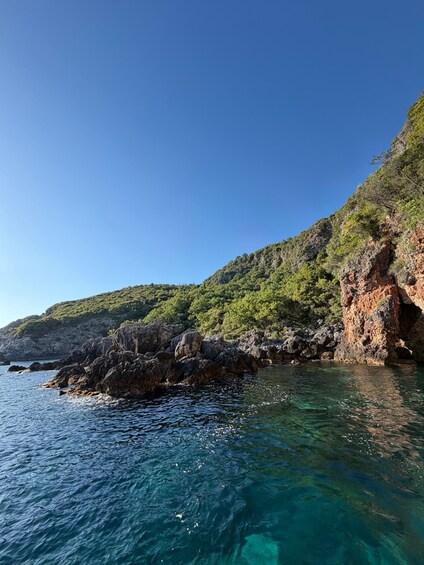 A coastal landscape with clear blue water, rocky cliffs, and green vegetation. 5