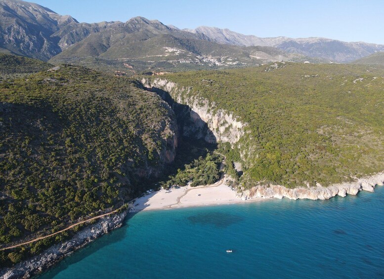 A coastal landscape with a beach, a clear blue sea, and a mountainous backdrop. 4