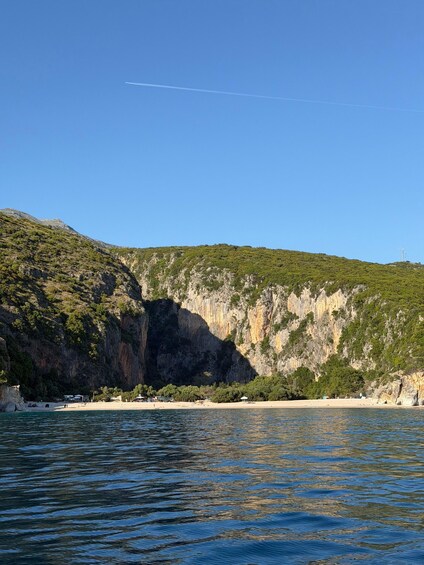 A coastal landscape with a rocky cliff, a beach, and calm water. 1