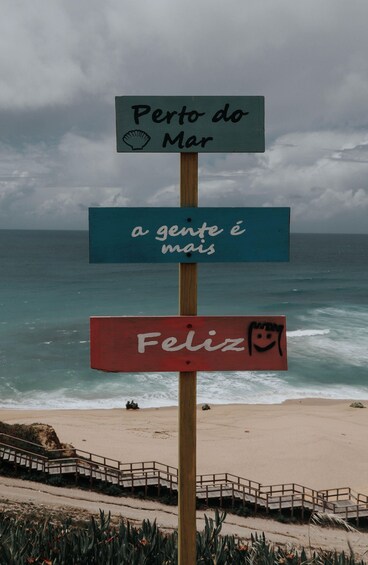 A beach with a wooden signpost displaying Portuguese phrases. 2