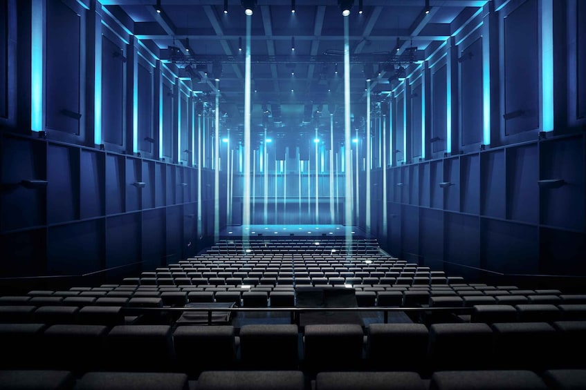 An indoor auditorium with rows of seats and blue lighting. 1