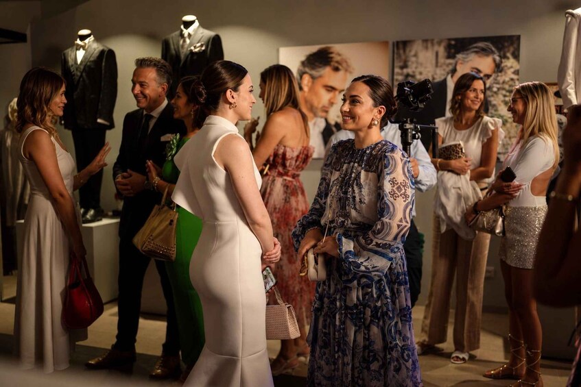 A group of people at an indoor event, some holding handbags and a camera. 3