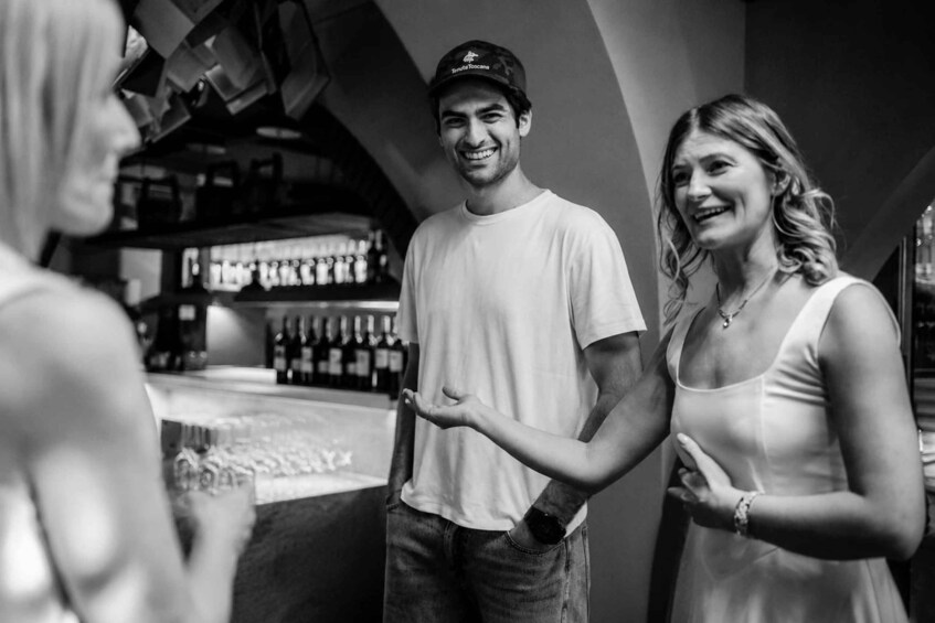A person in a white t-shirt and cap, standing in a bar with shelves of bottles. 4