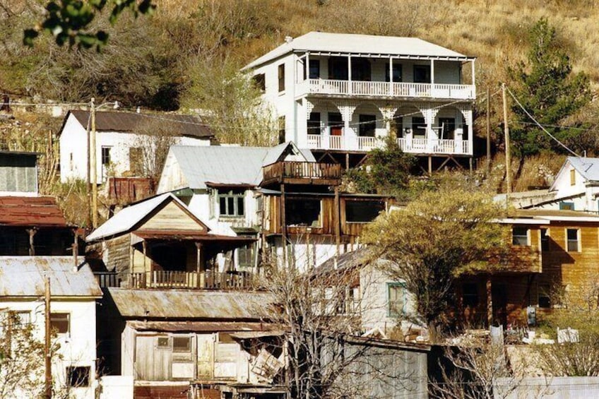 A cluster of old wooden houses with a prominent white building with a balcony on a hillside. 4