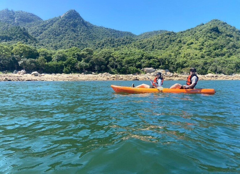 Two people kayaking on a calm river with mountains in the background. 1