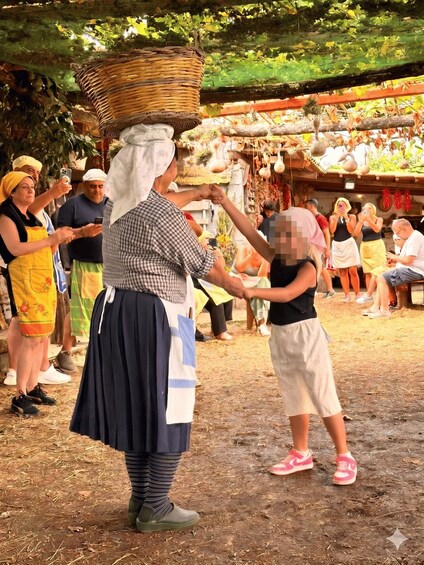 A person in traditional attire dancing with a child in an outdoor setting with a rustic backdrop. 3