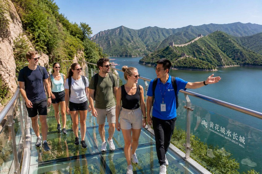 A group of people walking on a glass bridge with a scenic view of mountains and a body of water. 2