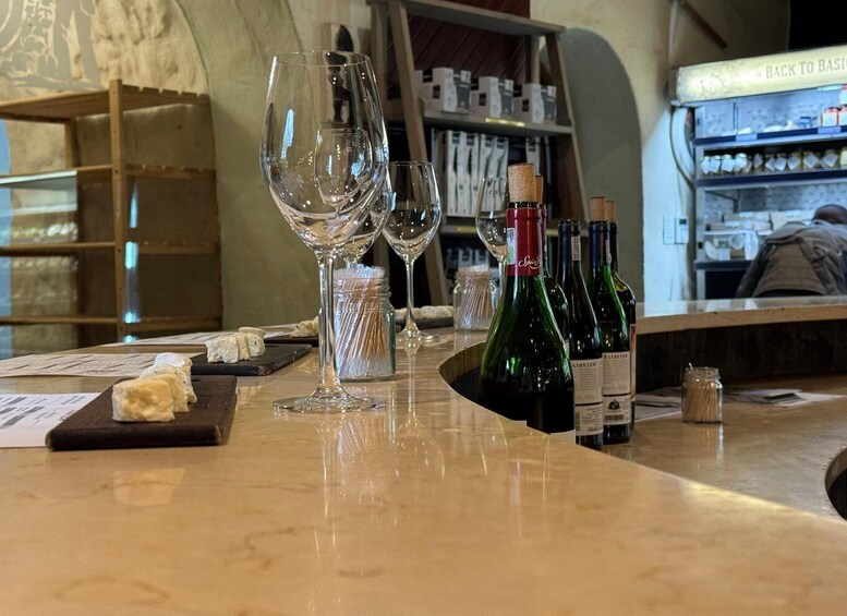 A bar with wine glasses, bottles, and cheese on the counter. 5