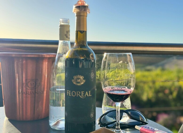 A bottle of Floréal wine, a glass of red wine, and a copper bucket on a table with a scenic view in the background. 4