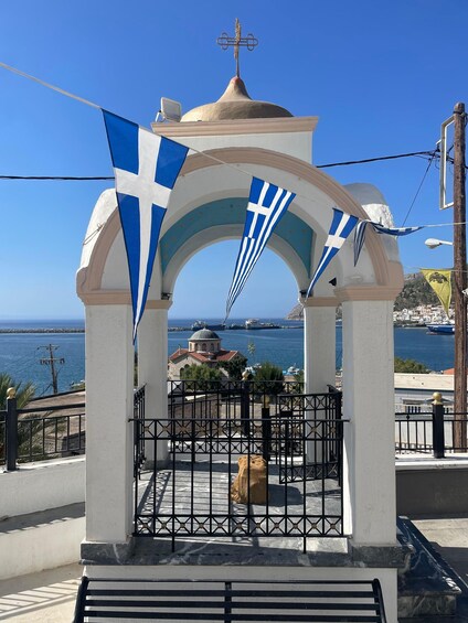 A white gazebo with blue and white flags, overlooking a coastal town with a clear blue sky. 5