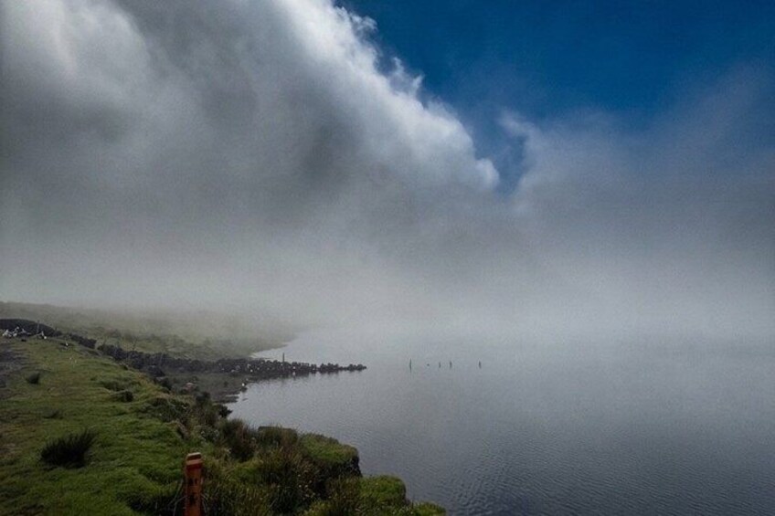 A calm lake with a misty shoreline, a distant shoreline with buildings, and a clear sky above. 5