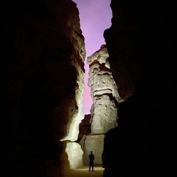 A person standing in a narrow canyon with a rock formation in the center. 5