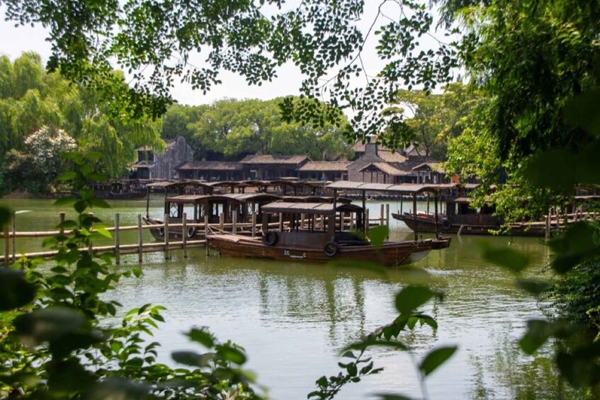 A calm river with wooden boats docked at a pier, surrounded by lush greenery and traditional buildings. 1